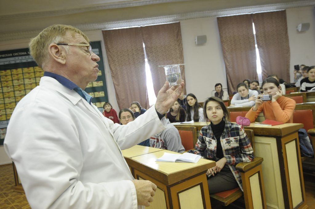 Кандидат химических наук Михаил Рябов показывает опыты слушателям проекта «Университетские субботы». Волшебным образом фиолетовая жидкость в колбе становится бесцветной. Фото: Пелагия Замятина, «Вечерняя Москва»